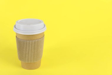 Sarı arka planda plastik kapaklı kağıt bardak, metin için boşluk. Kahve hazır.