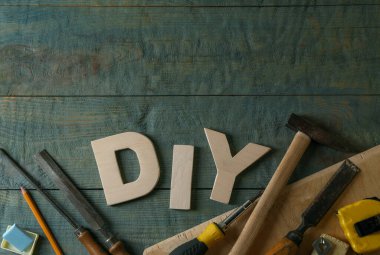 Gri ahşap masa üzerinde harflerden ve farklı aletlerden oluşan kısaltma DIY düz yatıyordu. Metin için boşluk