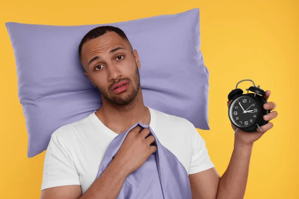 Tired man with pillow and alarm clock on orange background. Insomnia problem
