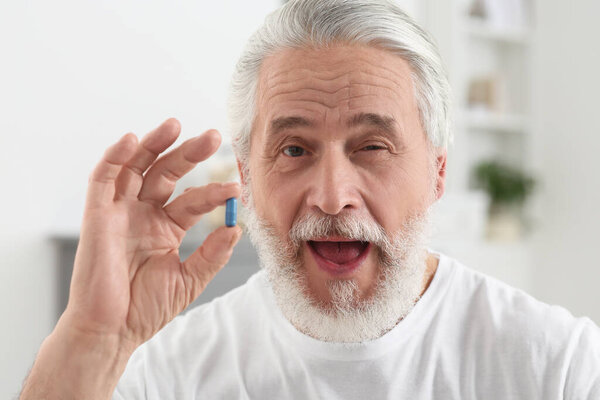 Handsome senior man with pill on blurred background