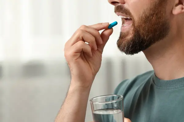 stock image Man with glass of water taking pill indoors, closeup. Space for text