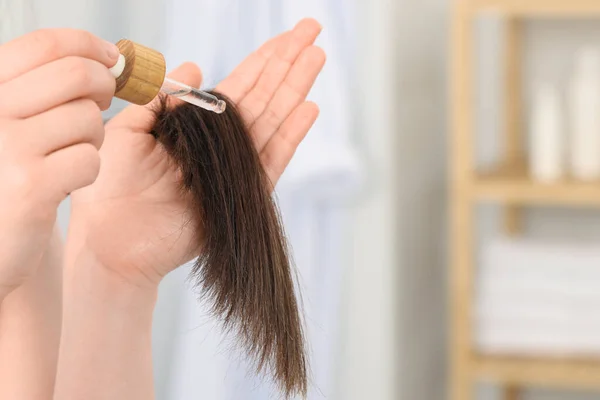 Woman applying essential oil onto hair indoors, closeup. Space for text