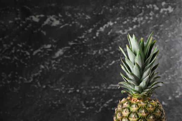 Whole ripe pineapple near black wall, closeup. Space for text
