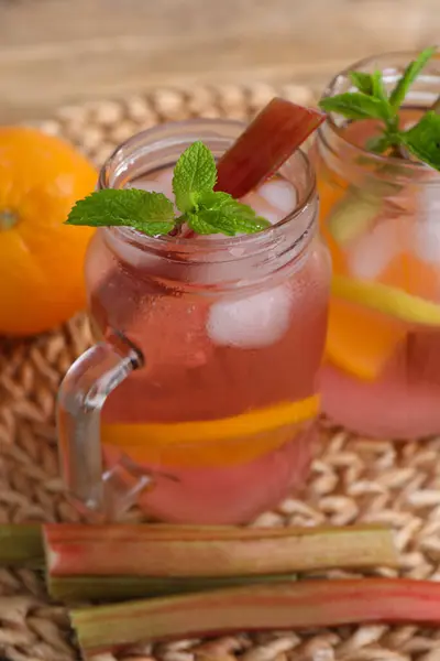 Mason jars of tasty rhubarb cocktail with citrus fruits on table