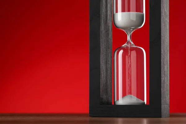 Hourglass with flowing sand on table against red background, space for text