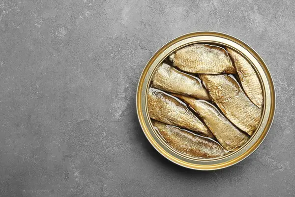 Sprats in tin can on grey textured table, top view. Space for text