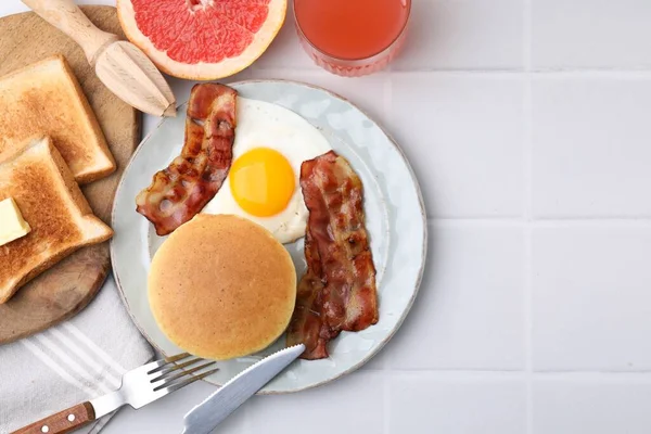 Tasty pancakes with fried egg and bacon served on white tiled table, flat lay. Space for text