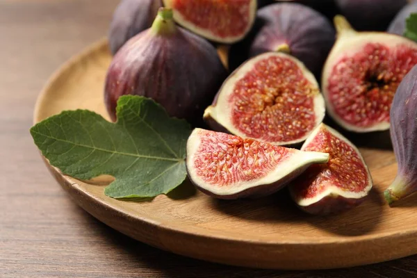 Whole and cut ripe figs with leaf on wooden table, closeup
