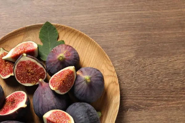 Whole and cut ripe figs with leaf on wooden table, top view. Space for text