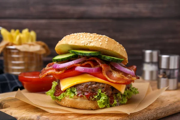 Tasty burger with bacon, vegetables and patty on wooden board, closeup