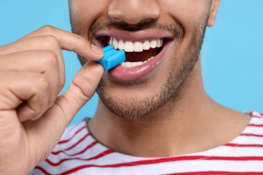 Açık mavi arka planda sakızlı mutlu adam, yakın plan