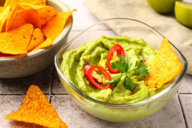 Bir kase lezzetli guacamole biberli, cips ve limonlu beyaz fayanslı masa, yakın plan.