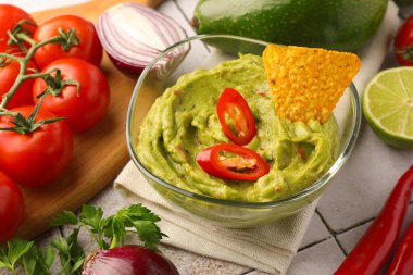 Bir kase lezzetli guacamole, cips ve malzemeler beyaz fayanslı masada, yakın plan.