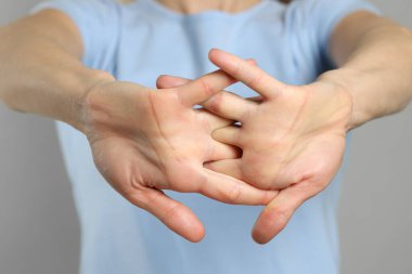 Açık gri arka planda parmak eklemleri çatırdayan kadın, yakın plan. Kötü alışkanlık.