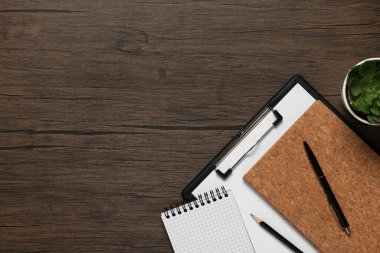 Farklı kırtasiye malzemeleri ve ahşap masadaki yeşil ev bitkisi, yazı için yeri olan düz bir yer. Merkez Ofis