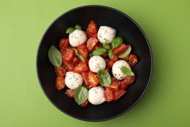 Domatesli Caprese salatası, mozzarella topları ve yeşil arka planda fesleğen.