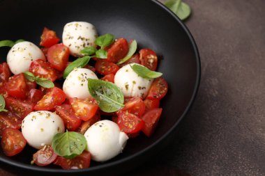 Domatesli Caprese salatası, mozzarella topları ve kahverengi masada fesleğen, yakın plan.