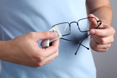 Gri arka planda mikrofiber bezle bardakları silen adam, yakın plan.