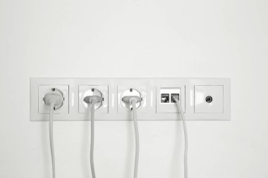 Beyaz duvarda fiş, ethernet ve TV coax plakalı birçok güç prizi var.