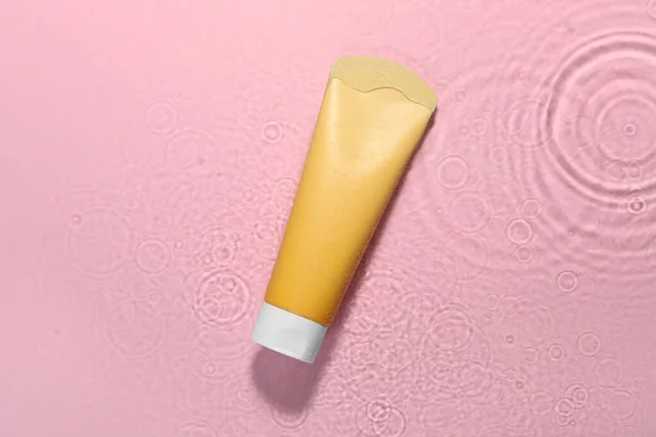 Tube of facial cleanser in water against pink background, top view