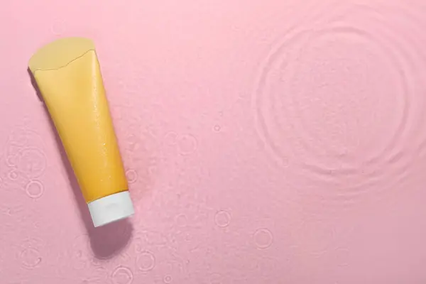 Tube of facial cleanser in water against pink background, top view. Space for text