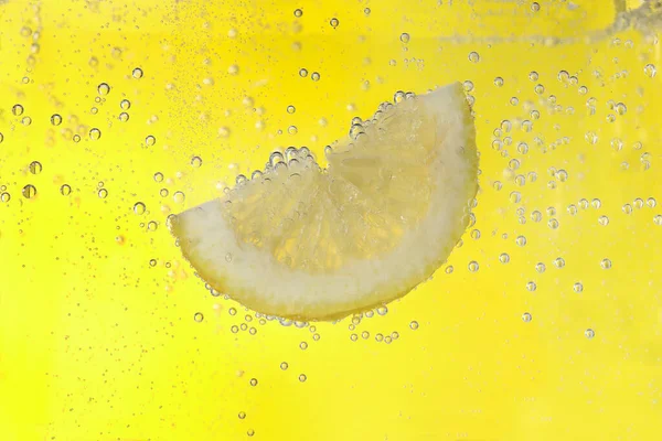 Juicy lemon slice in soda water against yellow background, closeup