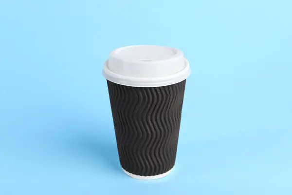 Brown paper cup with plastic lid on light blue background. Coffee to go