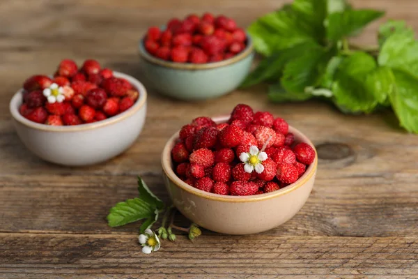 Fresh wild strawberries and flowers in bowls on wooden table
