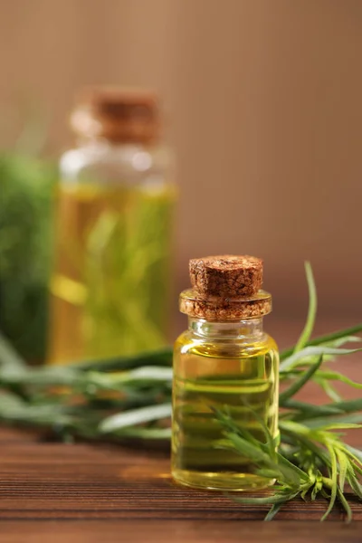 Bottle of essential oil and fresh tarragon leaves on wooden table
