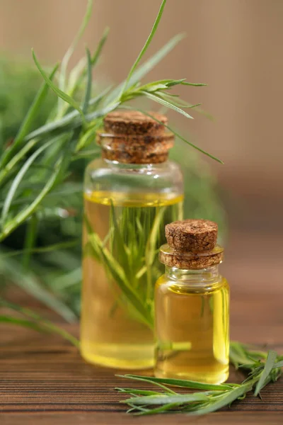 Bottles of essential oil and fresh tarragon leaves on wooden table