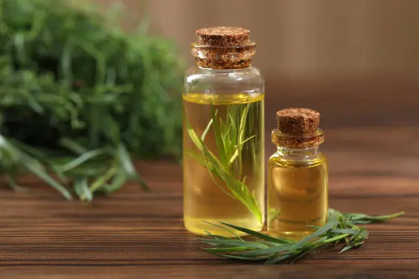 Bottles of essential oil and fresh tarragon leaves on wooden table