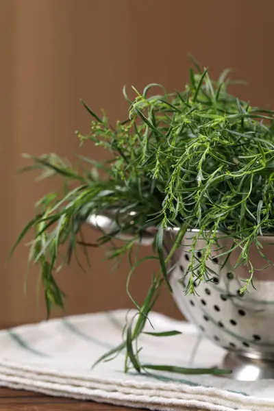 Colander with fresh tarragon leaves on wooden table, closeup