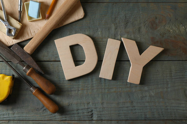 Abbreviation DIY made of letters and different tools on grey wooden table, flat lay