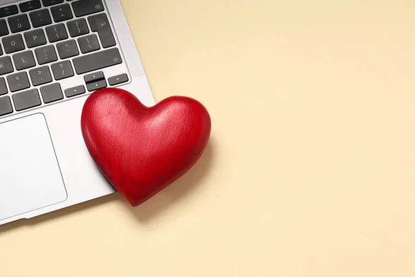 Long-distance relationship concept. Laptop and decorative heart on beige background, top view with space for text
