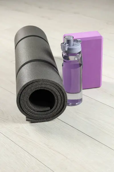 Exercise mat, yoga block and bottle of water on light wooden floor