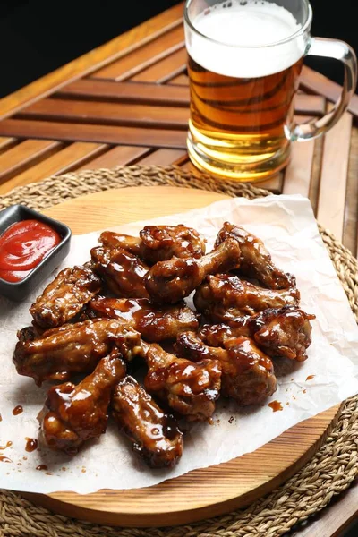 Tasty chicken wings, mug of beer and ketchup on wooden table. Delicious snack