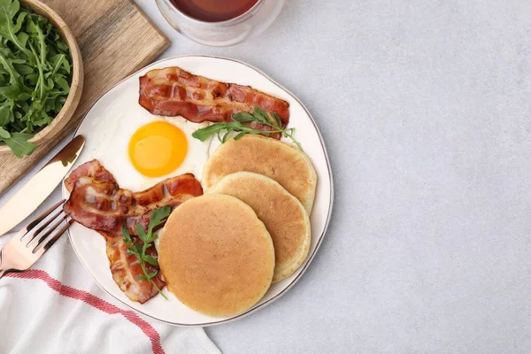 Tasty pancakes with fried egg and bacon served on light grey table, flat lay. Space for text