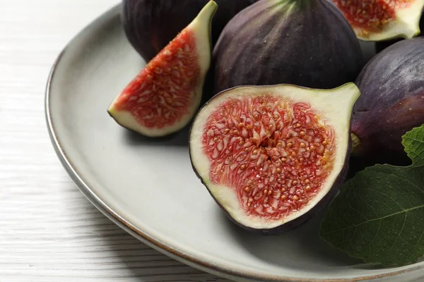 Whole and cut ripe figs with leaf on white wooden table, closeup