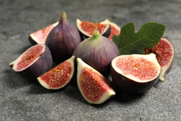 Whole and cut ripe figs with leaf on grey textured table, closeup