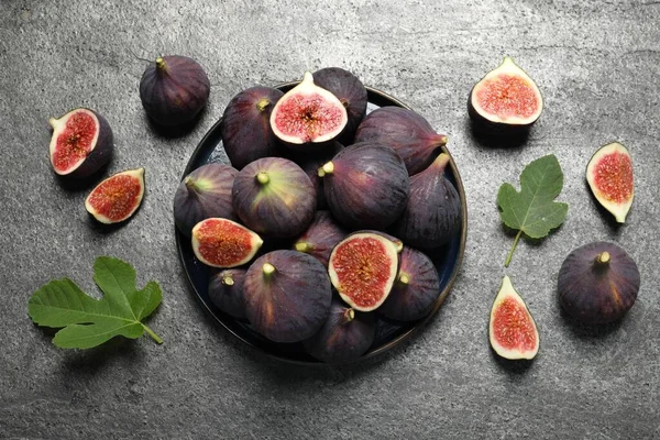 Whole and cut ripe figs with leaves on light grey textured table, flat lay