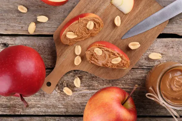Fresh apples with peanut butter and knife on wooden table, flat lay