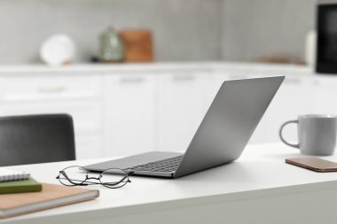 Merkez ofis. Dizüstü bilgisayar, gözlük, akıllı telefon ve kırtasiye malzemeleri mutfaktaki beyaz masada.