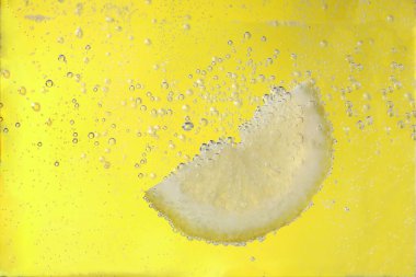 Sarı arka planda soda ile sulu limon dilimi, yakın plan.