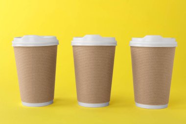 Sarı arka planda beyaz kapaklı kağıt bardaklar. Kahve hazır.