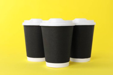 Sarı arka planda beyaz kapaklı kağıt bardaklar. Kahve hazır.