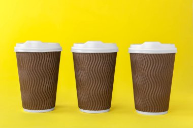 Sarı arka planda beyaz kapaklı kağıt bardaklar. Kahve hazır.