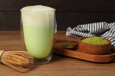 Bir bardak lezzetli matcha latte, bambu çırpısı ve ahşap masada yeşil toz, yakın plan.