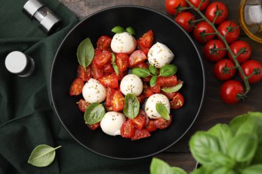 Domatesli Caprese salatası, mozzarella topları ve ahşap masada fesleğen.