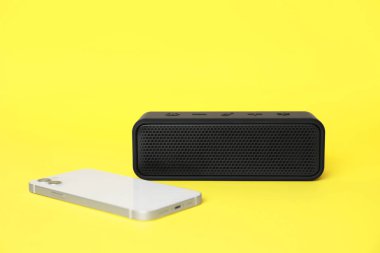 Portatif bluetooth hoparlör ve sarı arka planda akıllı telefon. Ses ekipmanları