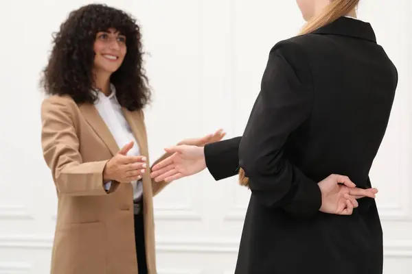 Employee crossing fingers behind her back while meeting with boss in office, closeup